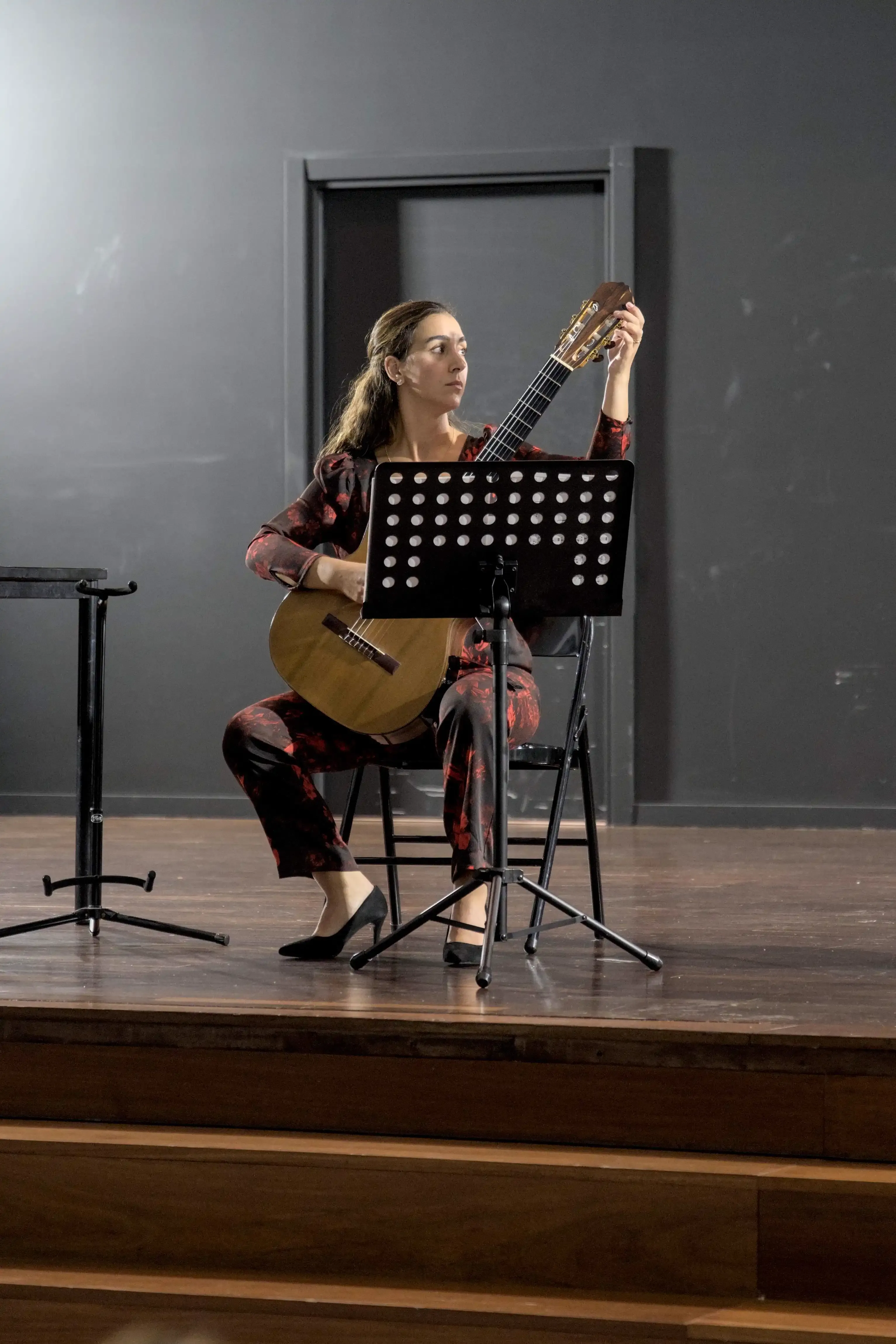 Uma mulher a afinar a guitarra clássica num palco.